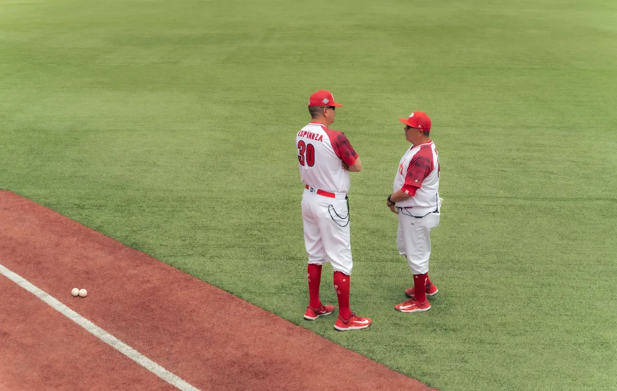Two baseball coaches in red and white uniforms discussing strategy on the field.