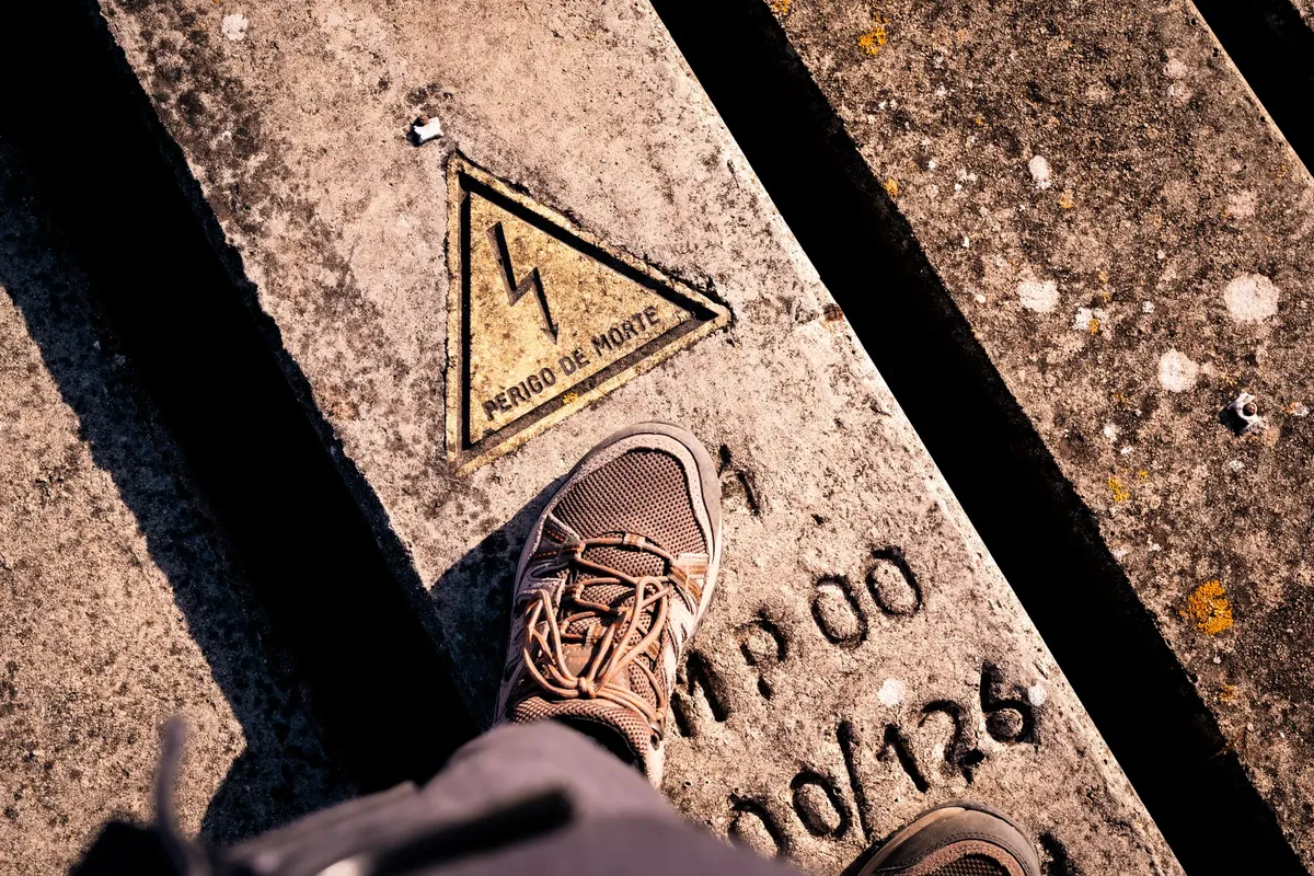 Foot on concrete slab with electrical warning sign in Portuguese.